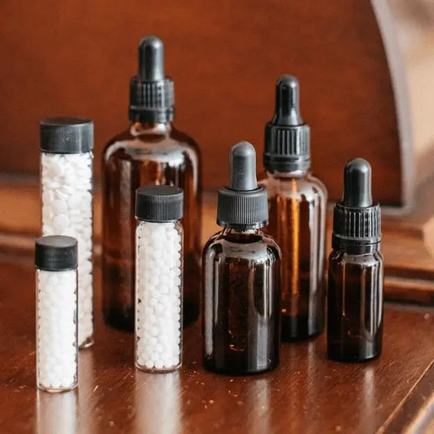 Bach™ Flower Mixing Bottles. There are 7 bottles in total: 4 droppers ( 1 big, 1 medium, 1 small, and 1 extra small) on the right of the image, and on the left, three bottles with pills( 1 big, 1 medium, and 1 small). All are on the wooden pharmacy counter.