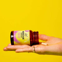 Yellow background an open hand holding the bottle of Rescue Balance & Positivity Capsules lying to the right and a capsule on top of the hand.