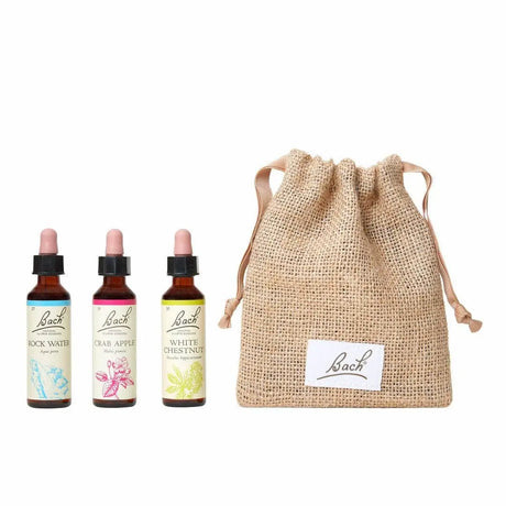There are three dropper bottles with  essences from the left to right: Bach™  Original Flower remedies Rock Water, Bach™  Original Flower Remedies Crab Apple and Bach™  Original Flower Remedies White Chestnut. Next to the last essence there is a burlap bag with the Bach™  logo on it.