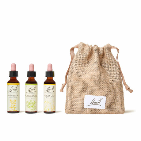 There are three dropper bottles with essences from left to right: Bach™ Original Flower Remedies Gentian, Bach™ Original Flower Remedies Honeysuckle and Bach™ Original Remedies Wild Oat. Nest to the last essence there is a burlap bag with the Bach™ logo on it.