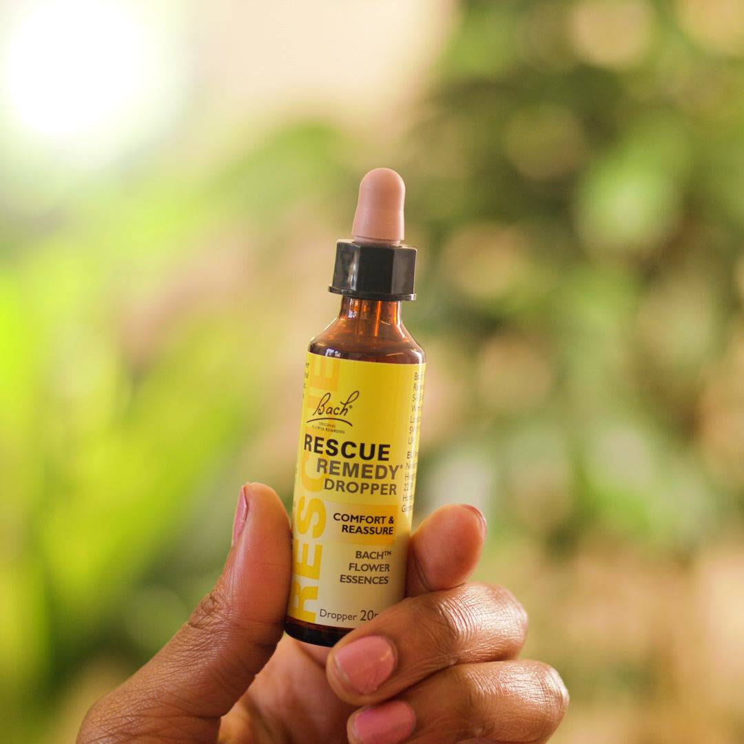 blurred background of a green tree and a hand holding a dropper of RESCUE® Remedy 10ml in the front of the picture 