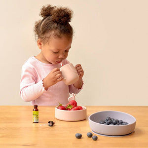 A little girl drinking water next to the bowls of fruit and  the kids dropper glycerine