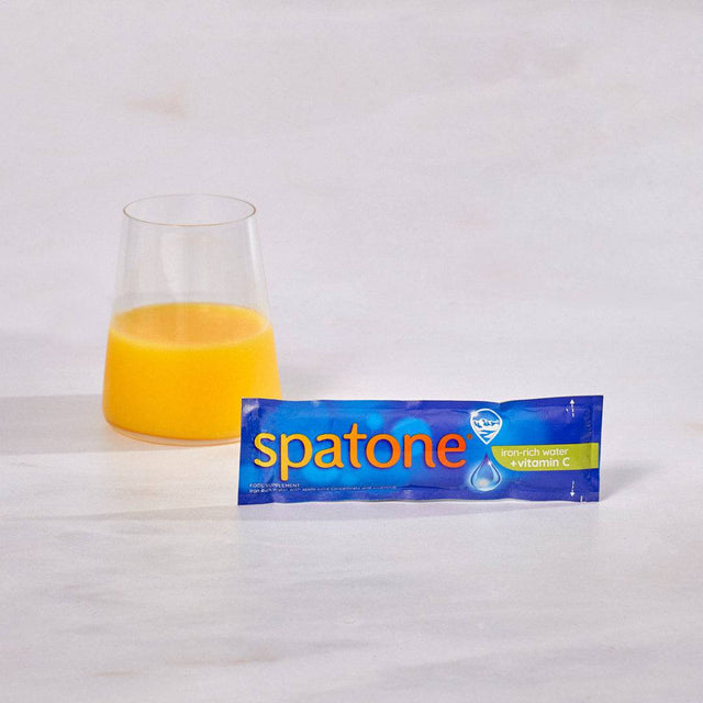 One sachet of Spatone at the front of a glass of orange juice