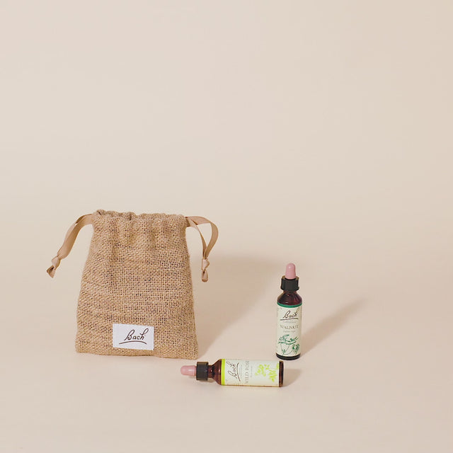 A hand taking out the Bach™ Original Flower Remedy Wild Oat dropper  from a burlap  bag and placing it next to the Bach™ Original Flower Remedy Walnut dropper  and Bach™ Original Flower Remedy Wild Rose dropper which is lying down.