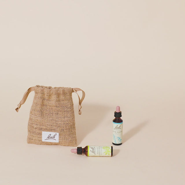 A hand taking out the Bach™ Original Flower Remedy Crab Apple dropper  from the burlap  bag and placing it next to the Bach™ Original Flower Remedy Rock Water dropper  and Bach™ Original Flower Remedy White Chestnut dropper which is lying down.