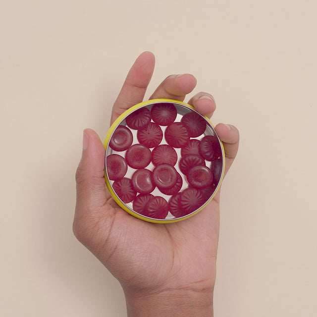 A hand holding RESCUE® Pastilles Blackcurrant opened tin and with the right hand taking first one pastille and second later the second pastille.