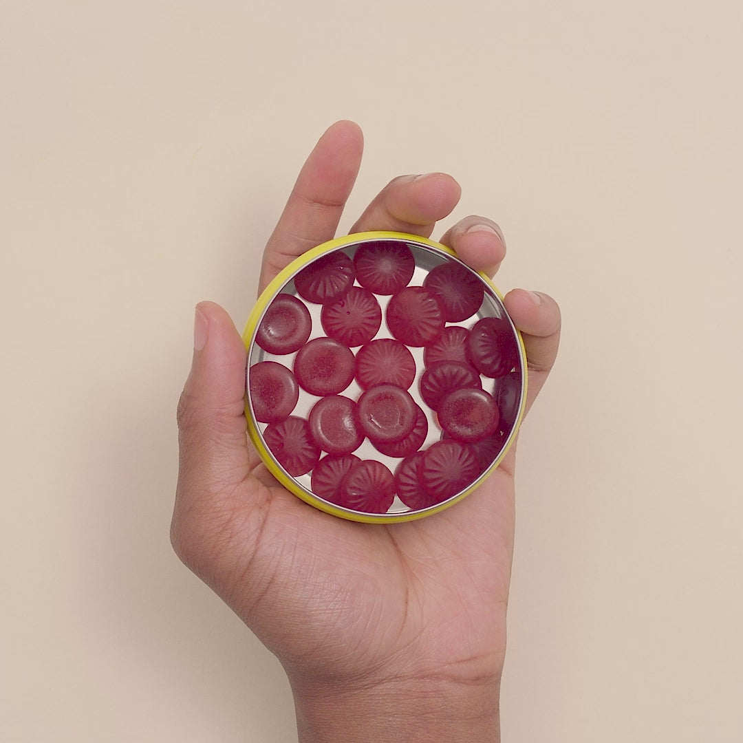 A hand holding RESCUE® Pastilles Blackcurrant opened tin and with the right hand taking first one pastille and second later the second pastille.